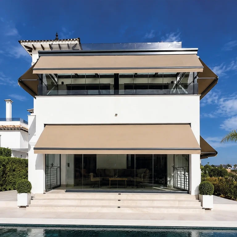 Toldos Cronos beige en dos plantas de una vivienda blanca con terrazas acristaladas junto a una piscina.