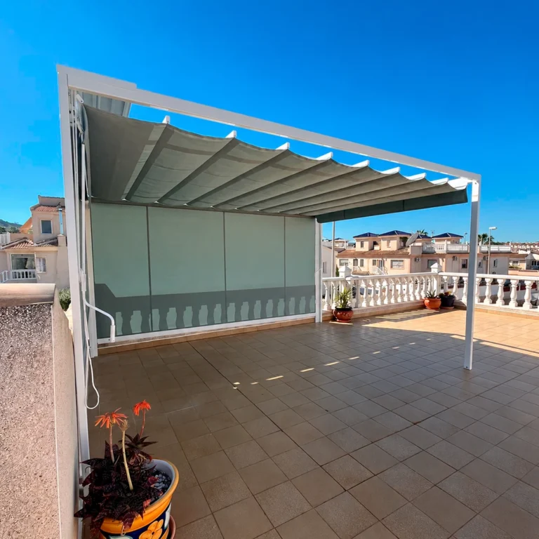 Toldo Solaris OPC gris con estructura blanca y cierre lateral sobre una terraza con balaustrada y macetas.